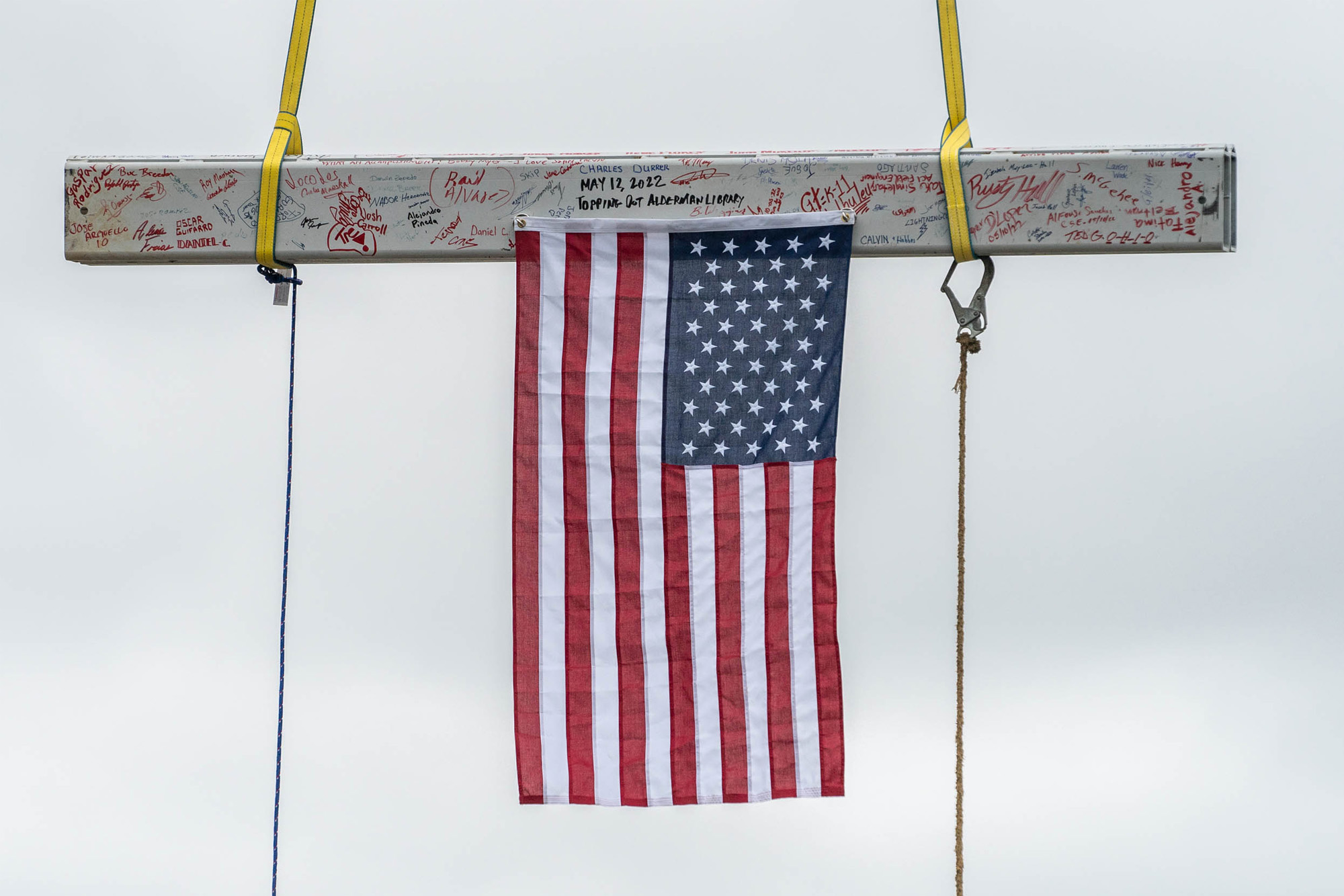 signed beam with American flag is hoisted into the air by a crane