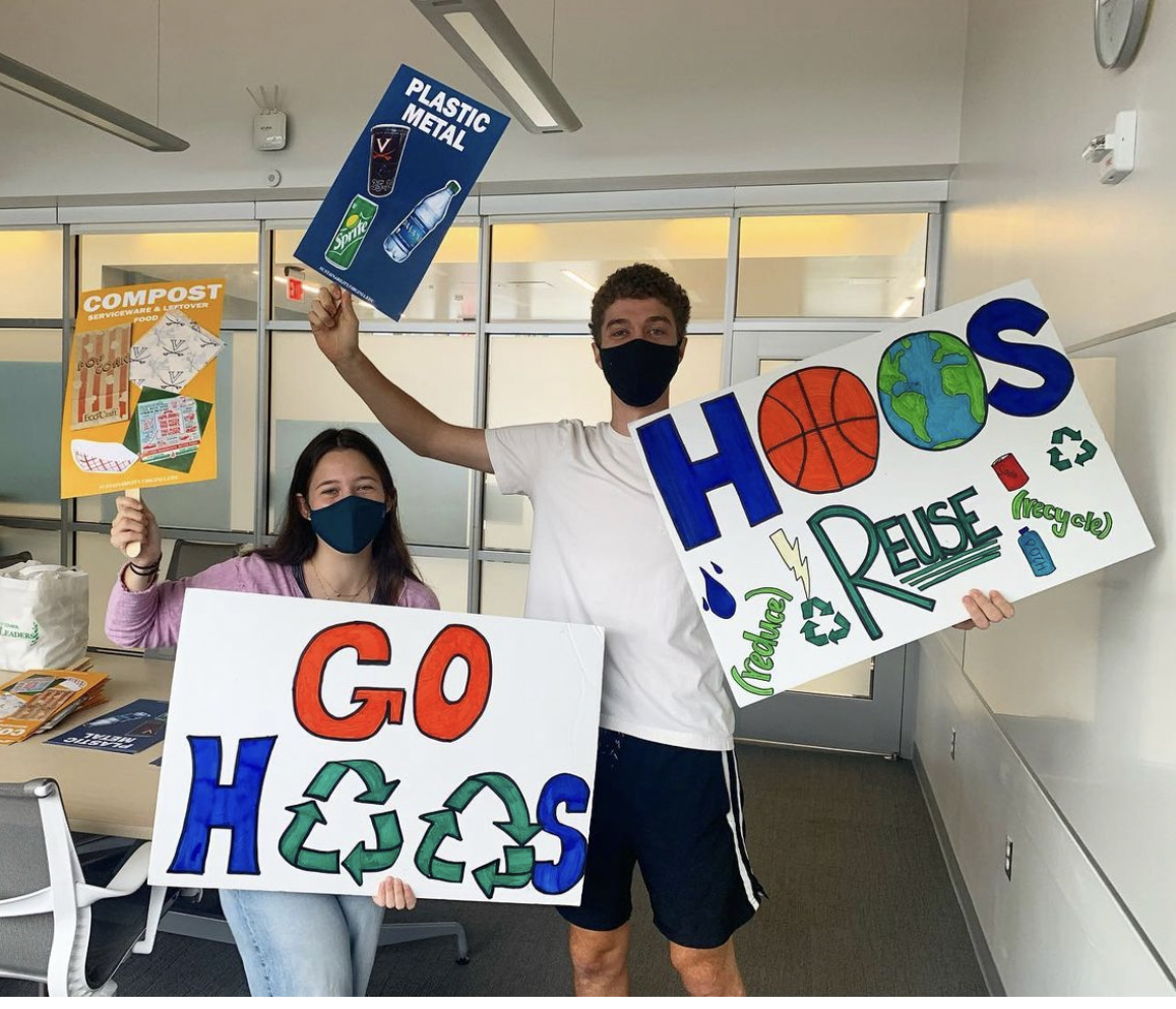 two students holding Go Hoos signs with recycling symbols