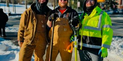 Group of three Facilities Management Crew members pausing their work shoveling snow from a sidewalk on Grounds. 