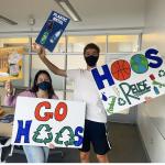 two students holding Go Hoos signs with recycling symbols